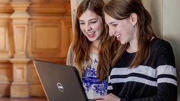 两个女学生拿着笔记本电脑大笑